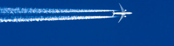 Flygplan med kondensstrimmor mot blå himmel